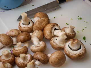 Washed champignon mushrooms on a cutting board with a knife. Cooking pasta with mushrooms and bacon. Classic Italian cuisine.