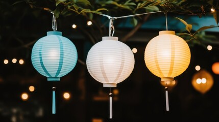 Obraz premium Three colorful paper lanterns hang from a tree branch, lit up and glowing in the evening.