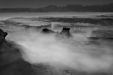 Misty ocean waves over rocky formations in black and white.