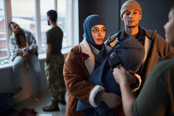 Waist up portrait of Middle Eastern refugee couple with baby talking to microphone while giving interview in shelter, copy space