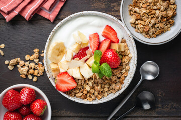 Granola bowl with greek yogurt, strawberries and banana slices on a wooden background, table top view of a healthy delicious breakfast or snack