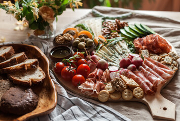 a person serving charcuterie board a platter of meat cheese crackers nuts olives and vegetables