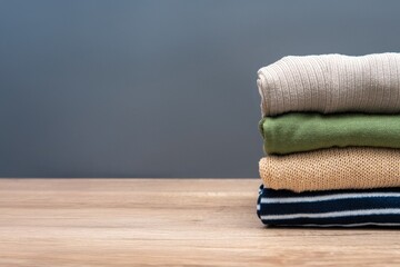 A stack of neatly folded clothes on a wooden table against a gray background. Copy space for text.