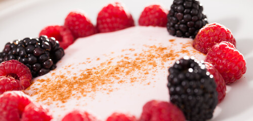 Raspberries and blackberries laid out on a white plate in circle with yogurt and cinnamon