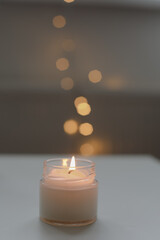 Cozy home interior decor, burning candle on table against blurred lights. Handmade scented soy wax candle in a glass. space for text. 