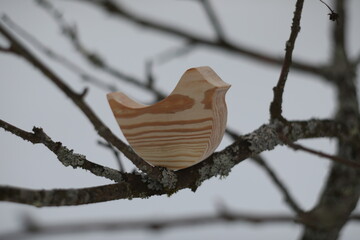 Wooden handmade toy bird on the tree branch on a winter day. Hello Spring concept. Winter landscape. Helping animals feed.