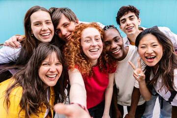 Diverse group of teenage student friends taking selfie portrait standing together over blue background. Youth and education concept