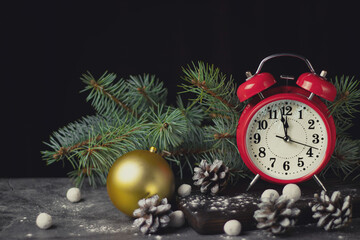 Red retro alarm clock with fir branches and a Christmas tree toy. The clock shows a few minutes until New Year.