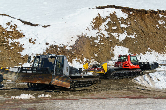 Two snow compactors. Grey Ratrak Prinoth Everest at left and red modern snowcat Pistenbully 600 at right. Dombay, Karachay-Cherkessia, Russia - October 27, 2024