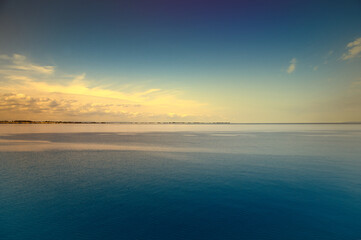 Tranquil seascape under a clear sky. The water reflects gentle clouds