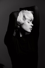 Elegant blonde woman in a black silhouette with raised arms, expressing confidence and grace against a dramatic dark background. Artistic portrait concept.