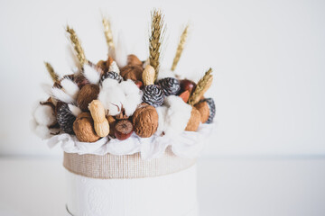 Beautiful handmade Christmas bouquet of nuts, pinecones and cotton flowers in round gift box against white background. Holiday floral decor.