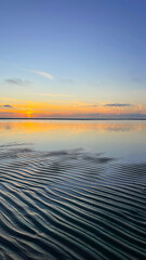 Natural background. Sunset on the shore of the mole. Low tide. A marine pattern on the sand. Calm. The landscape. Landscape. The sky is reflected in the water.
