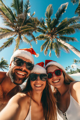 Happy young friends wearing Santa’s hats and Christmas sunglasses takes a selfie on the beach against the backdrop of palm trees. Winter holidays in exotic resort, travel photo in a tropical paradise