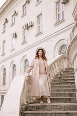 woman in elegant coat and hat against an intricate architectural backdrop, harmoniously blending modern fashion with historical allure. The soft daylight adds to its timeless appeal.