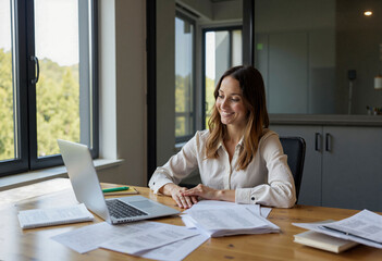 Smiling businesswoman working on laptop with documents in modern office