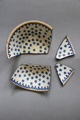A close-up of a broken ceramic vessel, each fragment uniquely shaped with delicate edges, evoking a sense of lost beauty and fragility. Blue dots pattern on the four pieces.