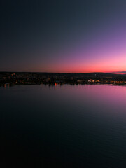 A stunning dusk view over a calm body of water, with a vibrant pink and purple gradient sky reflecting on the surface and city lights in the distance.