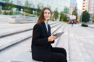 Fototapeta premium Young Professional Woman Sits on Steps in Urban Setting, Working on Tablet During Daytime