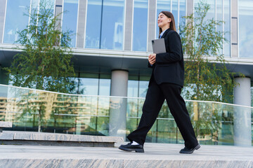 A Businesswoman Walks Confidently Outside a Modern Office Building During Daytime in the City