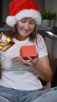 Woman in Santa hat sitting on sofa opening christmas gift. Frustration washes over her face as she opens contents inside, leading to moment of sadness, she is dissatisfied. vertical video