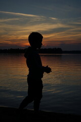 silhouette of a boy against the backdrop of sunset on the lake