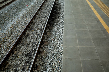View of a train tracks on ballast gravel and railway sleeper wood. A tiled platform is on the right.