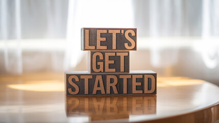 Three wooden blocks stacked display "LET'S GET STARTED" in bold, rustic font. Set on polished wood, with natural light through a window, it conveys motivation and readiness for a new beginning.