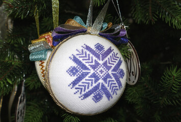 A Christmas ball with an embroidered snowflake in Ukrainian style hangs on a Christmas tree
