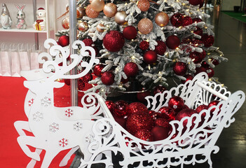Wooden reindeer stand carrying a bunch of red Christmas balls under a Christmas tree.