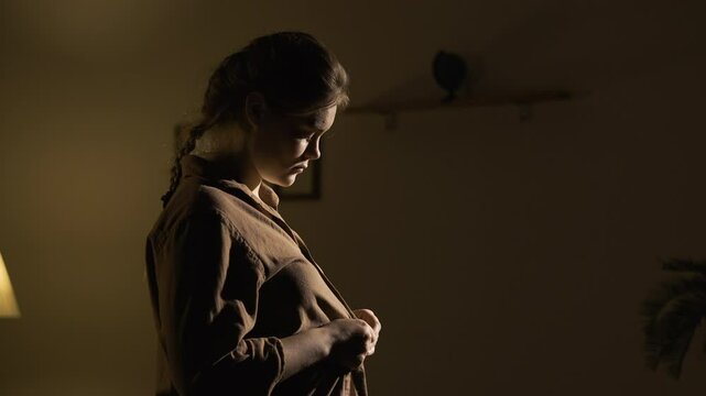 Woman unbuttoning and taking off brown shirt in evening in living room of house