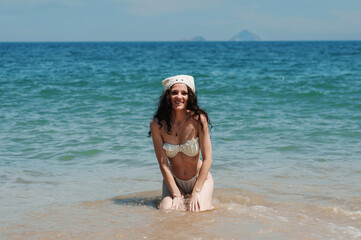 a young woman with a sexy body in a white swimsuit poses on the beach by the sea