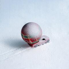 A miniature red car transports a large festive Christmas ornament across a snowy setting, creating a whimsical holiday scene filled with charm and creativity.