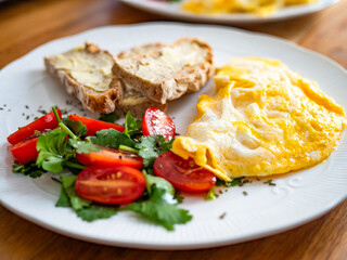 Continental breakfast - scrambled eggs, slice of bread with butter  and fresh vegetables on wooden table
