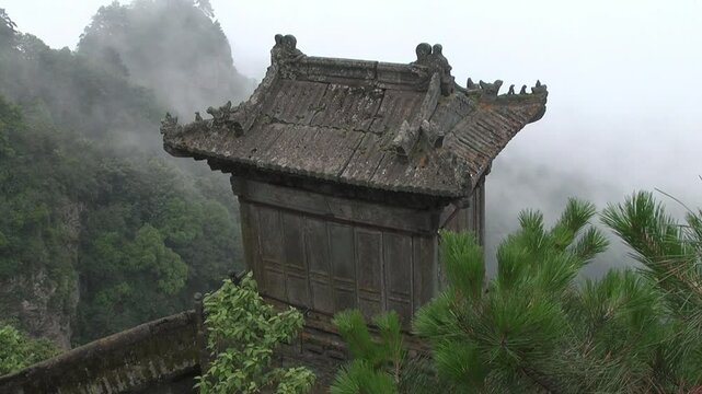 Ancient Taoist temple in the Wudang Mountains, China, partially shrouded in mist. The ornate rooftop and dense surrounding forest create a mystical, spiritual atmosphere.