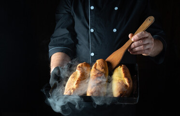 Warm, steamy loaves of bread are freshly baked and held by a chef in a dark kitchen. The golden...