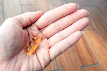three golden pills on palm. Hand withs yellow pills on wooden background. Vitamins And Supplements, Concept health benefits, nutrition, omega 3 and 6, sun, pain relief and vitamin D