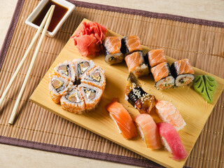 Sushi set with mix of sushi rolls with salmon, eel, tuna and shrimps on a wooden board decorated with wasabi and ginger