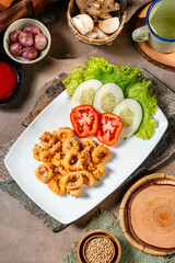 Crispy fried squid on a white plate with tomatoes, cucumber and lettuce
