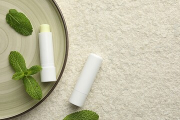 Mint lip balms and green leaves on beige textured background, top view. Space for text