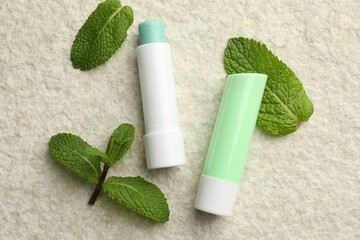 Mint lip balms and green leaves on beige textured table, flat lay. Cosmetic product