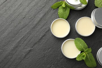 Mint lip balms and green leaves on black background, flat lay. Space for text