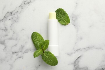 Mint lip balm and green leaves on white marble table, top view. Cosmetic product