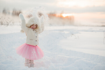 Winter lifestyle portrait of cheerful little girl in knitted sweater throwing snow in the air. Child is smiling and having fun in the snow park. Freedom and happiness concept.