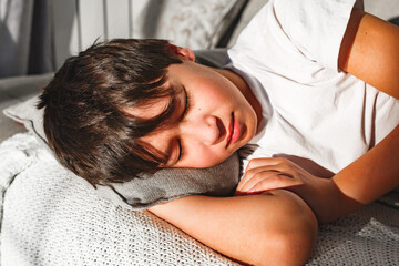 Cute tired boy sleeping in comfortable  sofa in beams of morning sun