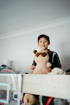 Pre-teen girl sitting on top of the bunk bed holding a plush toy.