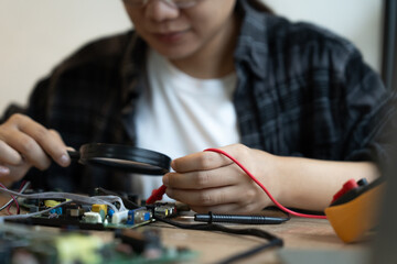 A woman is working on a circuit board with a magnifying glass. She is focused and determined to fix the problem