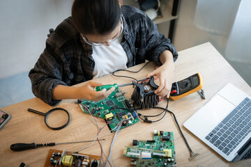 A woman is working on a computer part. She is wearing a white shirt and a black jacket