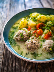 Boiled meatballs in dill sauce with potatoes and vegetables on wooden table
