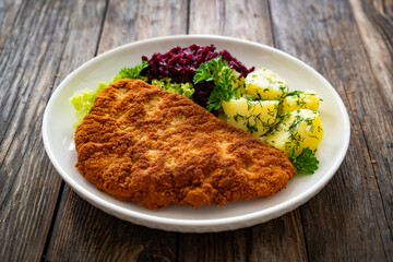 Crispy breaded fried pork chop, boiled potatoes and red cabbage served on white plate on wooden table
